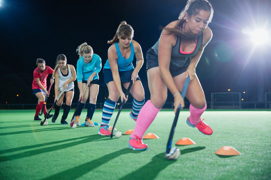 Determined female field hockey players practicing sports drill on field at night