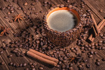 Background for coffee beans in dark color  background. Natural coffee beans arabica close-up macro. Сup of coffee beans wooden table with sprinkled coffee grains of cinnamon sticks and anise.