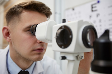 Close up portrait of male optometrist using refractometer machine while testing vision of unrecognizable patient