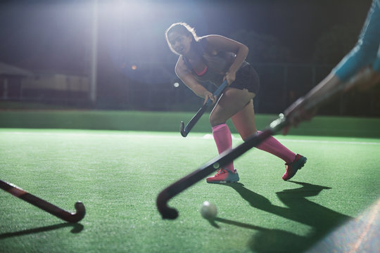 Young female field hockey running with hockey stick on field at night