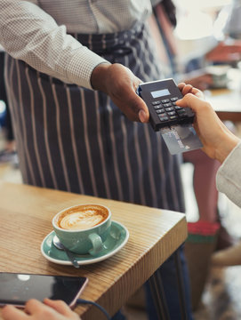 Customer paying waiter with credit card reader at cafe table