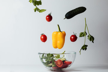 Healthy salad with flying vegetable ingredients on a white background. Cherry tomatoes, yellow pepper, cucumber, parsley