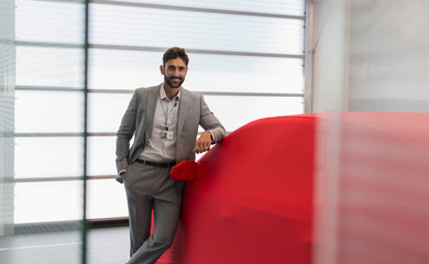 Portrait confident car salesman leaning on covered car in car dealership showroom
