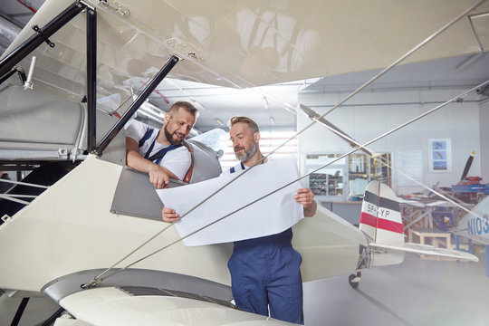 Male engineer mechanics examining plans at airplane in hangar