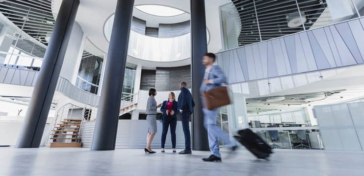 Business people talking pulling suitcase in architectural, modern office lobby