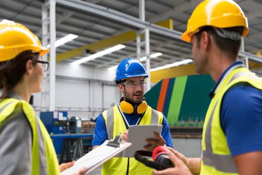 Supervisor and workers with clipboard and digital tablet talking in factory