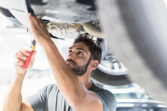 Focused male mechanic working under car in auto repair shop