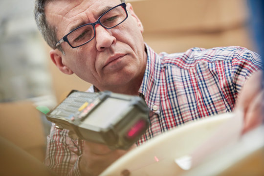 Focused male worker using IR code scanner in fiber optics warehouse