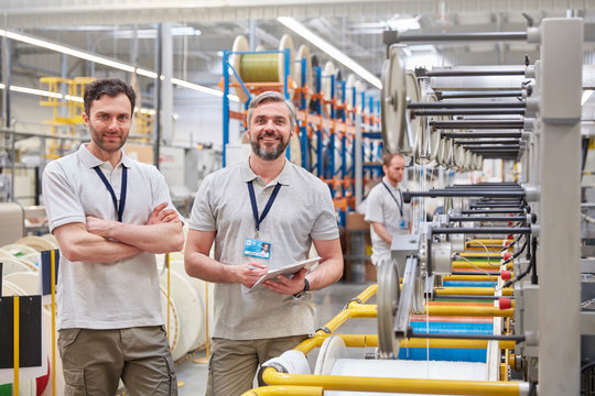 Portrait smiling, confident male workers digital tablet on fiber optics factory floor