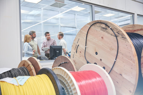 Supervisors talking in office behind spools in fiber optics factory