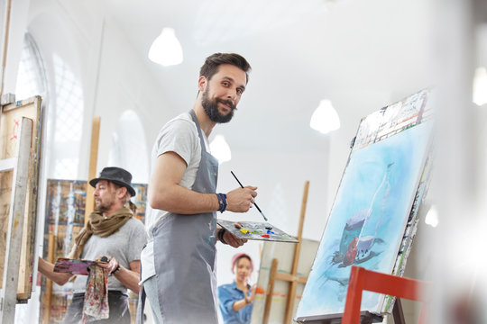 Portrait confident male artist painting palette in art class studio