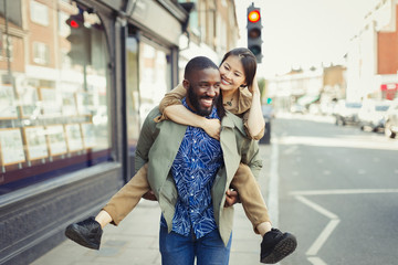 Playful young couple piggybacking on urban street
