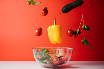 Healthy salad with flying vegetable ingredients on a red background. Cherry tomatoes, yellow pepper, cucumber, parsley.