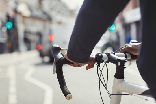Hands on man on bicycle handlebars, commuting on sunny urban street