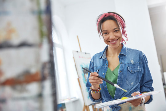 Portrait smiling female artist paintbrush palette, painting in art class studio