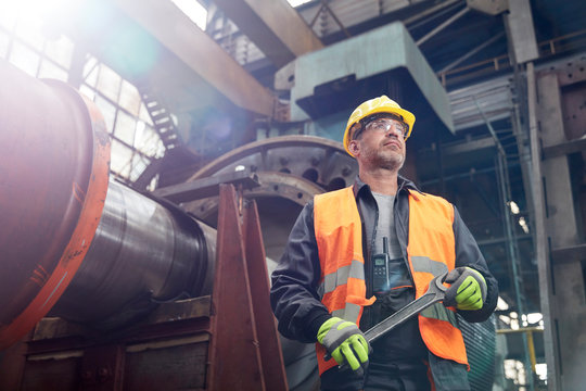 Confident male worker holding wrench in factory