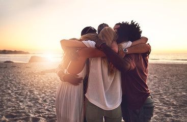 Young friends hugging in a huddle on sunset summer beach