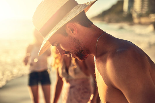 Young man in straw hat looking down on sunny summer beach