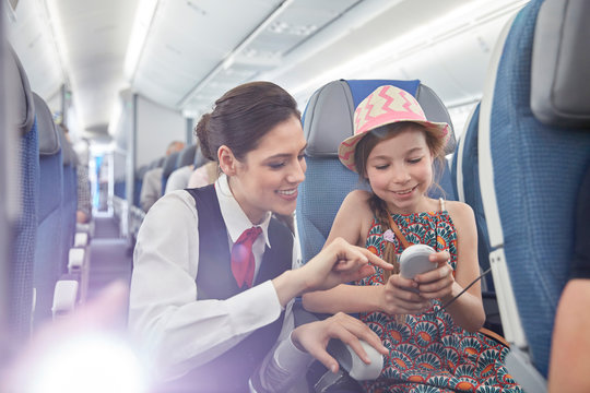 Flight attendant helping girl passenger remote control on airplane