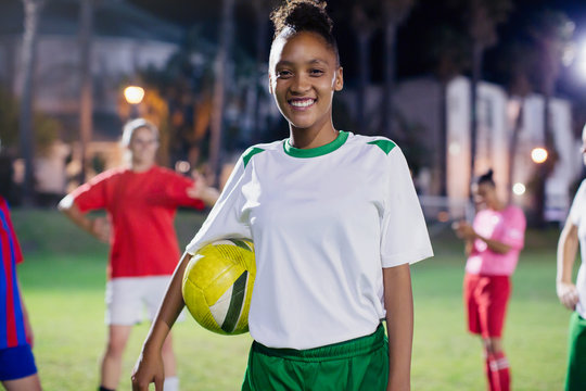 Portrait smiling, confident young female soccer player ball on field at night