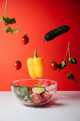 Healthy salad with flying vegetable ingredients on a red background. Cherry tomatoes, yellow pepper, cucumber, parsley.