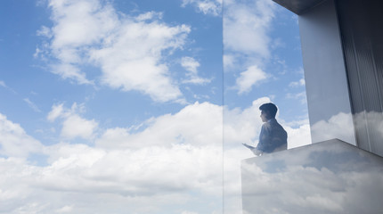 Pensive businessman standing on modern balcony looking at blue sky clouds