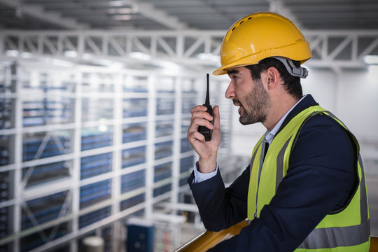 Male supervisor talking, using walkie-talkie on platform in factory
