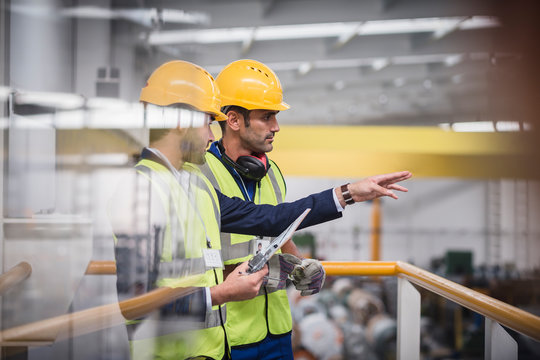 Male supervisors with clipboard talking on platform in factory