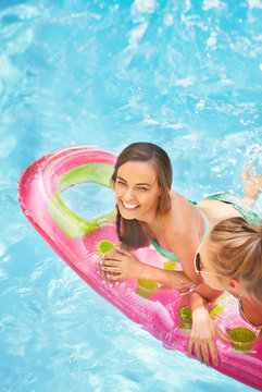 Portrait smiling women friends floating on pool raft in summer swimming pool