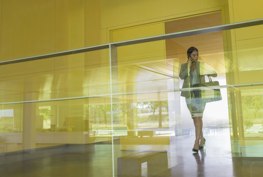 Businesswoman talking on cell phone checking wristwatch in modern office