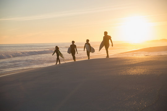 Silhouette family surfers walking surfboards on sunny summer sunset beach