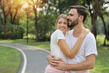 Young caucasian couple wearing white T-shirt standing and hugging in park outdoor during summer season. They looking away and smiling with happy face.(healthy or friendship valentine concept)