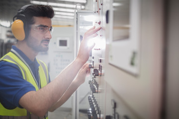 Male worker wearing ear protectors, operating machinery at control panel in factory