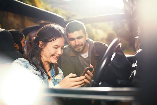 Young couple checking GPS on smart phone, enjoying road trip in jeep