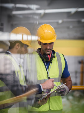 Male supervisor and worker with clipboard talking in factory