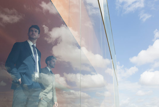 Pensive businessmen looking out modern office window at sunny blue sky clouds