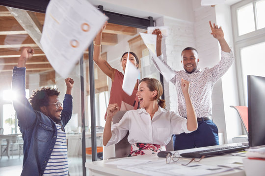Exuberant business people celebrating, throwing paperwork overhead in office