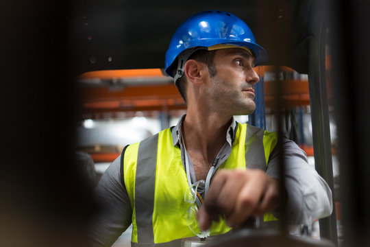Male worker driving forklift, looking over shoulder in factory