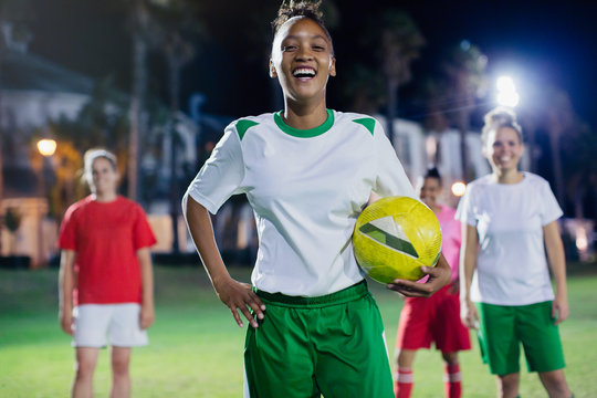 Portrait confident, laughing young female soccer player practicing on field at night