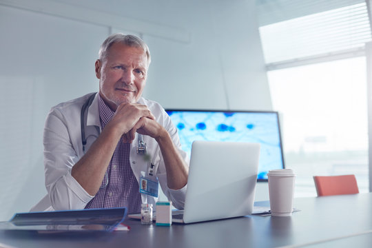 Portrait confident male medical scientist working at laptop in hospital