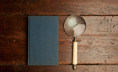 blue book with optical magnifying glass on old wooden table