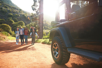 Young friends walking toward jeep on sunny dirt road in woods