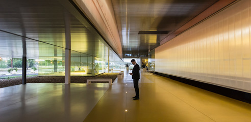 Businessman texting smart phone in illuminated modern office lobby corridor