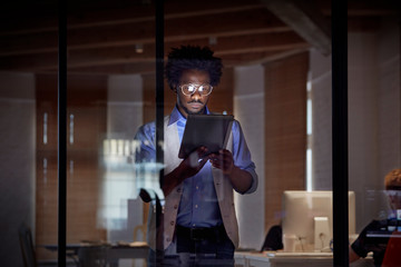 Design professional working late, using digital tablet in dark office at night