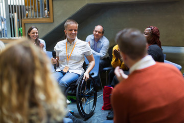 Audience smiling, listening to female speaker microphone in wheelchair