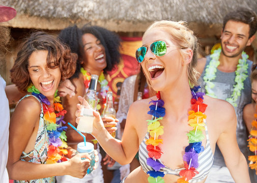 Playful friends wearing leis drinking and partying at sunny summer poolside
