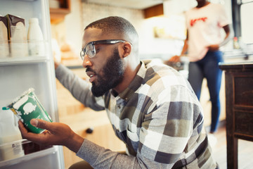 Young man reading label on container at refrigerator