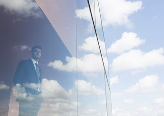 Businessman looking out modern office window at blue sky and clouds