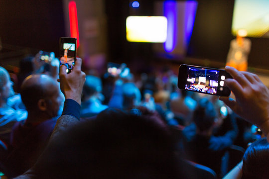 Audience with smart phones videoing conference
