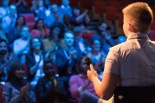Female speaker in wheelchair with microphone on stage talking to audience